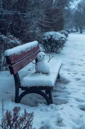 Snowman Sitting on a Snowy Bench in a Winter Park