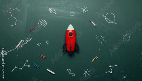 Rocket Model on a Chalkboard With Space-Themed Drawings and Paper Clips Aroun...