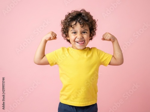 Funny little sportive kid boy in yellow shirt, showing his muscles. Happy strong nerd kindergarten child showing bicep. Dream, confidence, success, possible, innovation. Go back elementary school.