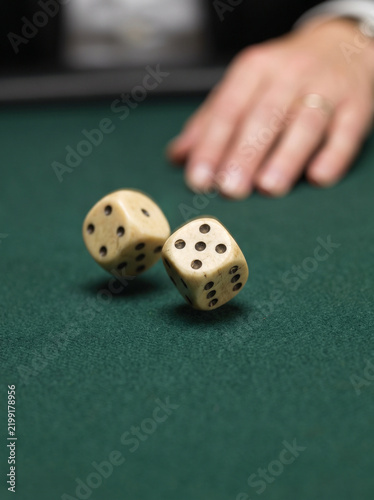 Two dice rolling on a green felt table with a hand in the background  