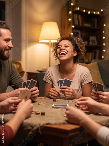 Friends laughing and playing cards around a cozy living room table  