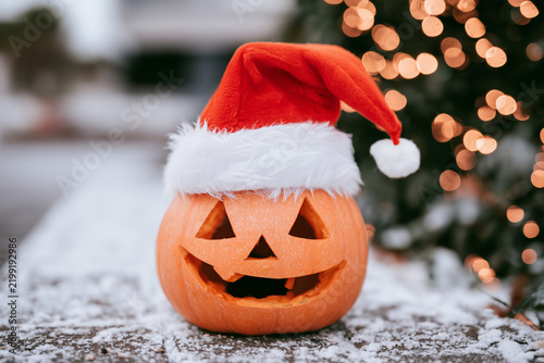 Pumpkin wearing Christmas hat near blurred lights