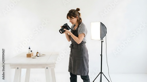 Woman photographing small cosmetic bottles on a white table in studio