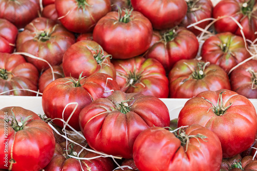 Fresh organic ribbed heirloom beefsteak tomatoes with green stems at a local farmers market