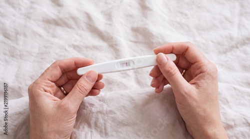 Pregnancy test positive hands bedroom fertility conception result detail home Hands examine a positive pregnancy test above white bedding at home for conception news and family planning campaigns