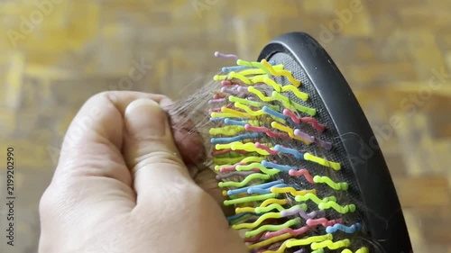Woman hand pulling a clump of loose hair from a black brush with colorful bristles. hair loss, alopecia problem, grooming routine, health care.