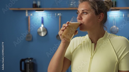 Slim woman in sportswear drinking smoothie, has weight loss diet enjoys healthy drink in kitchen. copy space