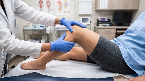 Physician examining patient knee during a medical consultation in a clinical office setting.