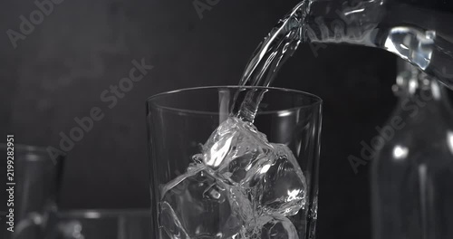 Water pouring into glass with ice cubes in slow motion on black background