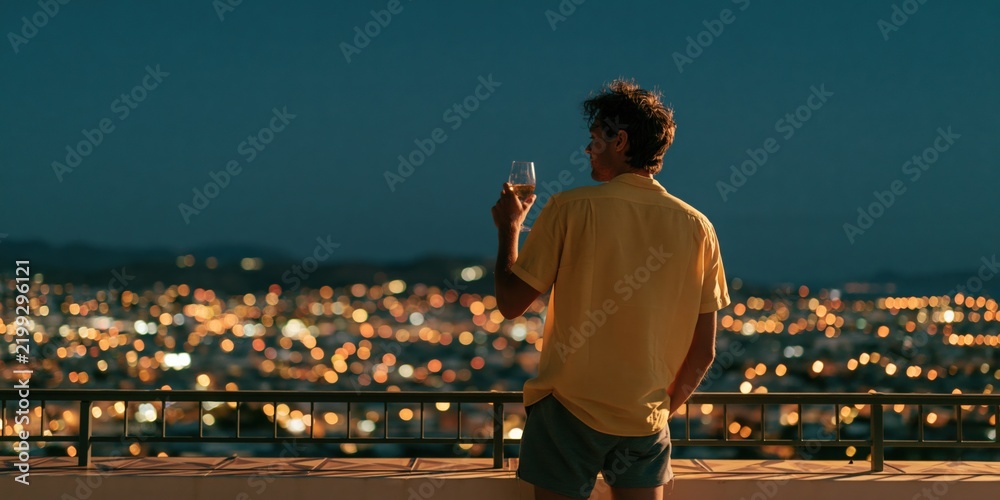Obraz premium Man on balcony overlooking city skyline at dusk with wine glass for background and banner design