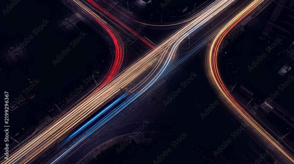 Obraz premium Colorful light trails at a city intersection captured at night, creating dynamic shapes.