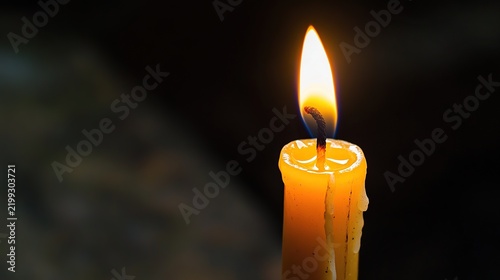Close-up of a single burning candle with a warm orange flame in darkness