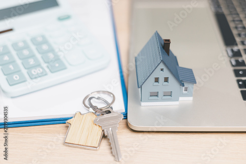 Fotografie Miniature house on a laptop beside keys and calculator represents digital mortgage services, online property buying, home loan planning, real estate finance, and modern home ownership