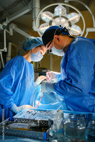 Surgeon and assistant performing surgery under operating room lights