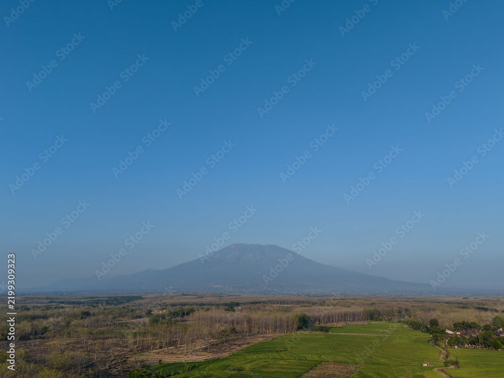 Fototapeta premium Scenic view of a majestic mountain under a clear blue sky, with lush green fields and rural landscape in the foreground.