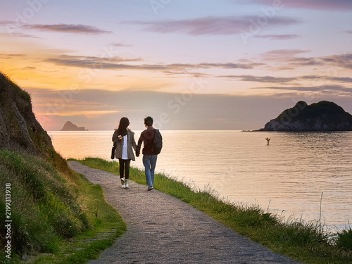 カップルが夕日を眺めて海岸道を歩く