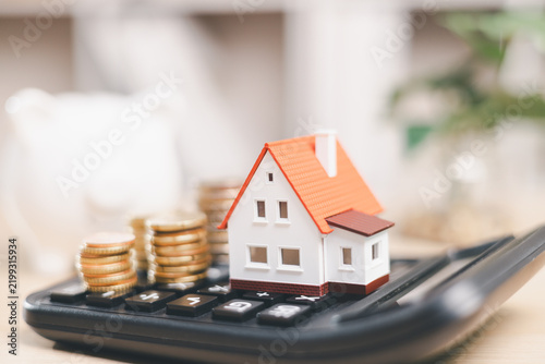 Obraz na płótnie Miniature house and coin stacks on a calculator symbolize mortgage calculation, home affordability, property costs, loan payments, interest rates, budgeting, and real estate finance planning