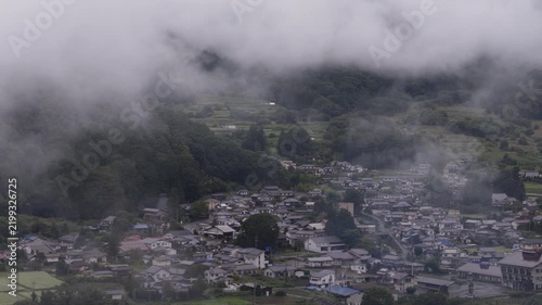 Fog and clouds move over small town at foot of green mountains in Nagano, Japan