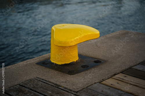 Bright yellow mooring bollard on concrete pier, maritime infrastructure, docking safety, harbour equipment, nautical travel industry