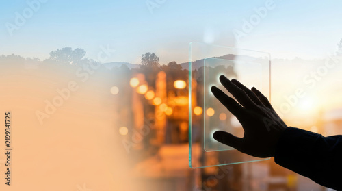 Silhouette hand touching glass panel against warm city light creates reflective technology scene with calm evening atmosphere