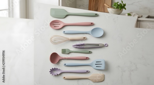 A top down view of various colorful silicone and wooden kitchen accessories arranged neatly on a clean white background surface