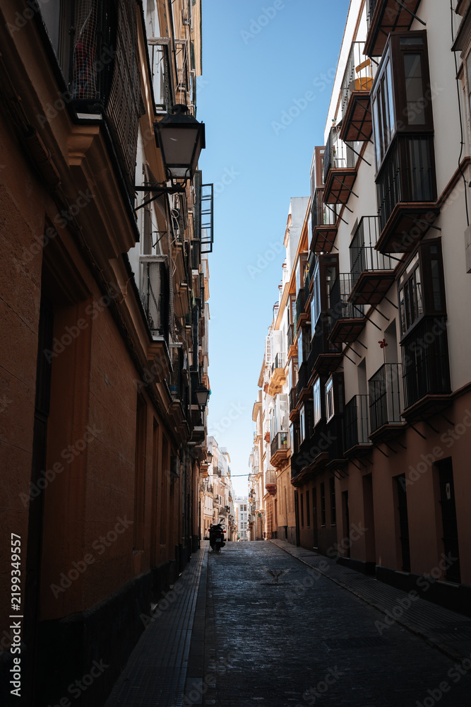 Fototapeta premium Narrow street with tall buildings and balconies under a clear blue sky