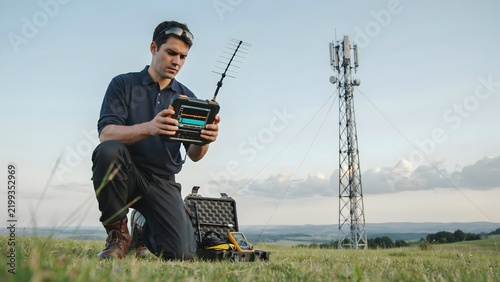 Technician Testing Signal Quality Near Cell Tower in Open Landscape
