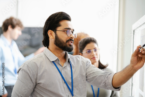 Diverse business professionals collaborating and discussing project strategy while reviewing information on a presentation board in a modern office.