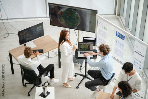 Diverse technology professionals collaborating around multiple computer screens and data dashboards while analyzing information and discussing business strategy.