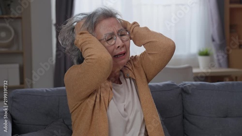 Distressed senior woman holding head feeling dizzy and weak in living room