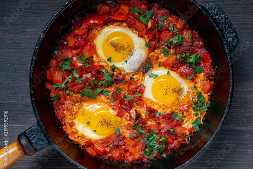 Traditional middle eastern shakshuka in cast iron skillet. Top view of traditional shakshuka with fried poached eggs in rich spicy tomato and bell pepper sauce topped with fresh parsley in pan