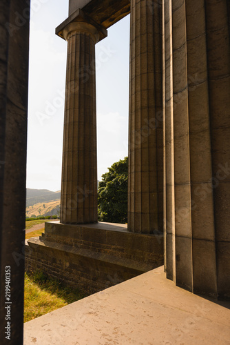 Foto Weathered stone columns in Edinburgh, Scotland frame rolling hills, trees, and warm daylight under bright sky at historic classical monument