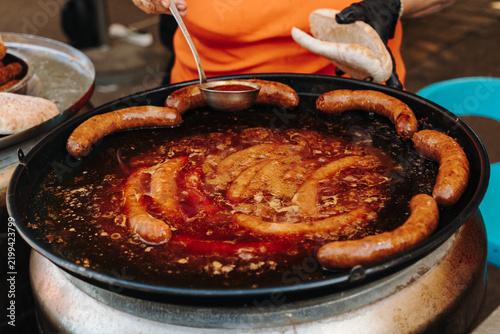 Fotografie Sausages simmer in a rich red sauce at a Balkan street food stall