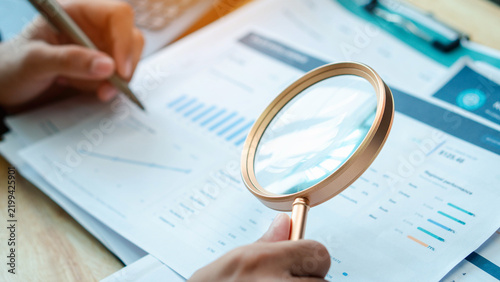 Accountant examines financial reports with a magnifying glass in an office. Business audit concept for document review, accounting analysis, compliance,  evaluation, and quality control.