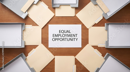 Eeo paper surrounded by folders and document trays on a desk representing equal employment opportunity