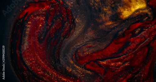 Ink spill. Sparkling fluid. Defocused yellow red colorful glitter mix acrylic texture floating on abstract art background.