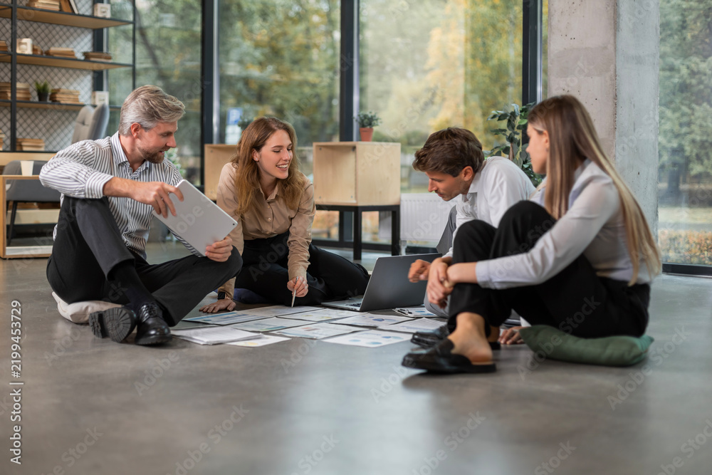 Fototapeta premium Group of young business people working on new project sitting with financial documents spread out on the floor