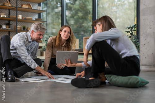 Business people looking at project plan laid out on floor, discussing new project plan in modern office.