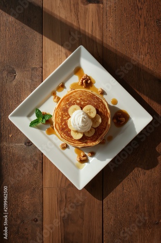 Pancakes Served With Bananas, Whipped Cream, and Walnuts on a White Plate