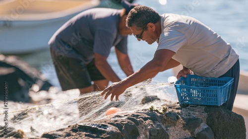 Frayed nylon net being hauled by a weathered fisherman onto a salt-crusted stone wall, showing a meager catch for fisheries