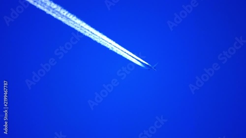 Airplane flying high in a clear blue sky leaving a long white contrail behind, high altitude view