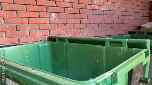 Man throwing a plastic garbage bag into a green dumpster outdoors against a brick wall. waste disposal, trash management, environment cleaning, everyday routine.