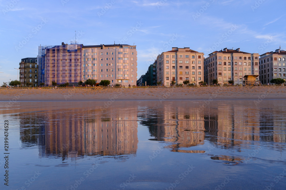 Obraz premium Sunset over Zurriola beach with city reflection on wet sand, San Sebastian, Basque Country, Spain