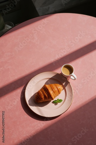 Croissant and Coffee on a Pink Table in a Bright Room in the Morning