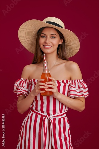 Woman in a Striped Outfit Holds a Drink and Smiles in Front of a Red Background