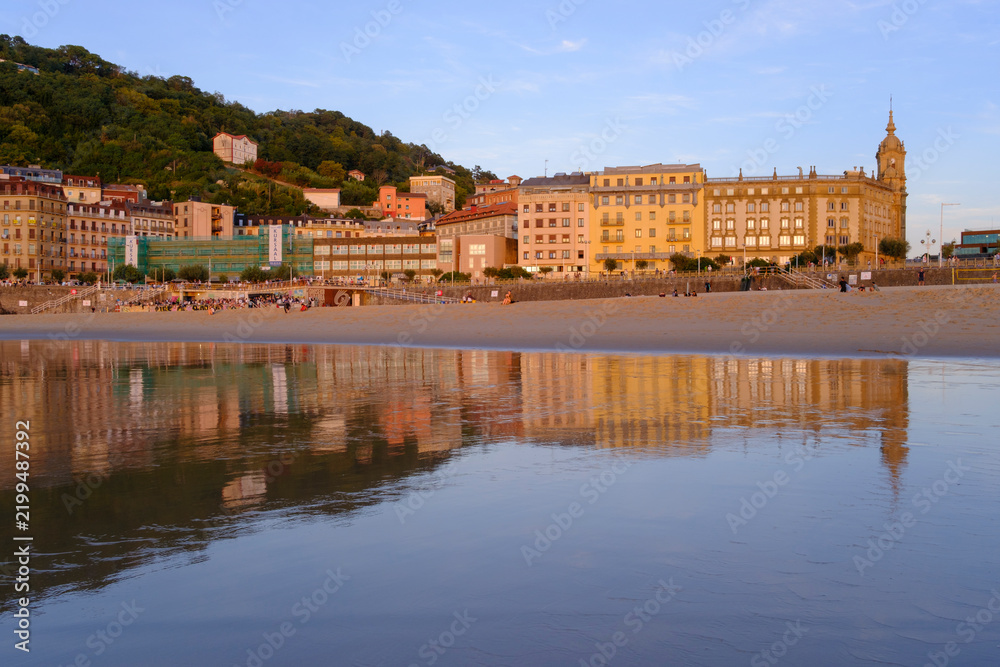 Obraz premium Sunset over Zurriola beach with city reflection on wet sand, San Sebastian, Basque Country, Spain