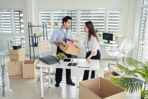 Young asian business coworkers packing and carrying cardboard boxes together during office relocation and moving into a new workplace
