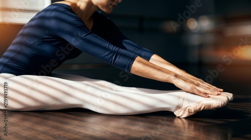 Close up of a ballet dancer stretching her legs in a leotard and tights in a dance studio.