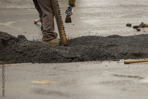 A construction worker using a metal rake to move asphalt. 