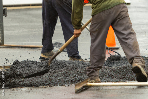 Two construction workers moving asphalt with shovels. 